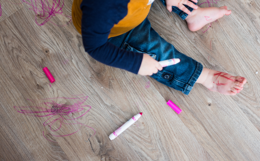Toddler holding marker sitting on wooden floor, pink marker scribbles on floor